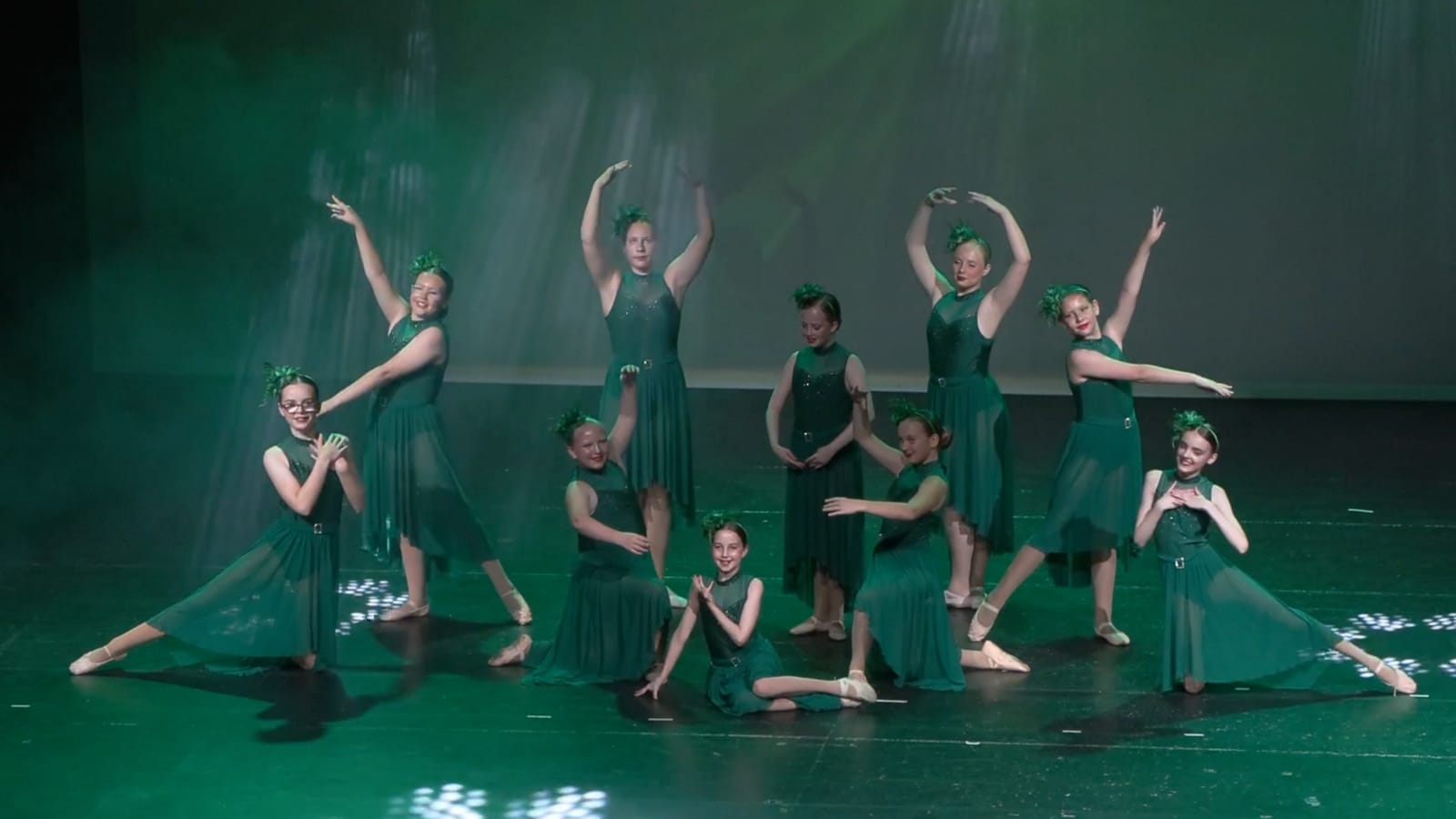 A group of dancers in green costumes posing on stage